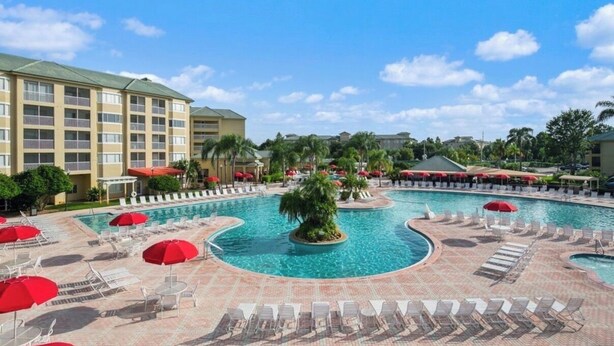 A hotel with a large pool area, multiple lounge chairs, and umbrellas. - Summer Disney Getaway, 2BR/2BA, sleeps 6, June 18-21, Resort Pool (Kissimmee)