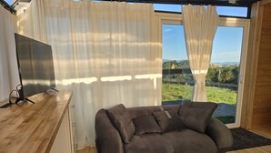 A modern living room with a sofa, a flat-screen TV, and a large window with curtains. - Cozy Luxury Cabin in the De Luz Heights (Fallbrook)