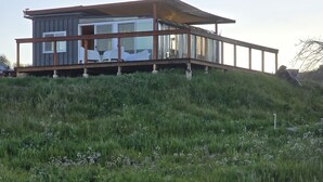 A modern house with a glass facade, situated on a grassy hill with a wooden deck. - Cozy Luxury Cabin in the De Luz Heights (Fallbrook)