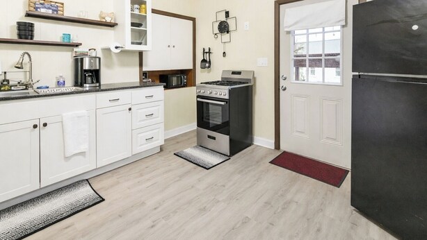 A compact kitchen with white cabinets, a stove, microwave, and a black refrigerator. - Spacious 2BR Apt Free Parking Baden (Baden)