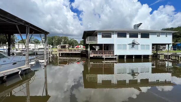Ein Anwesen am Wasser mit einem Haus auf Stelzen, einem überdachten Steg und Booten im Wasser.