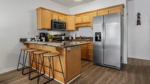 A modern kitchen with wooden cabinets, a stainless steel refrigerator, a microwave, and a bar stool area. - Entire home in Gulfport, Mississippi (Gautier)