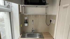 Una cocina compacta con un lavamanos integrado, un microondas sobre la encimera y un refrigerador pequeño debajo.