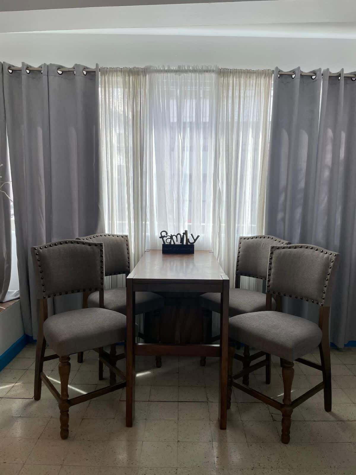 Un espace repas comprenant une table rectangulaire et quatre chaises rembourrées dont les dossiers sont décorés de boutons.