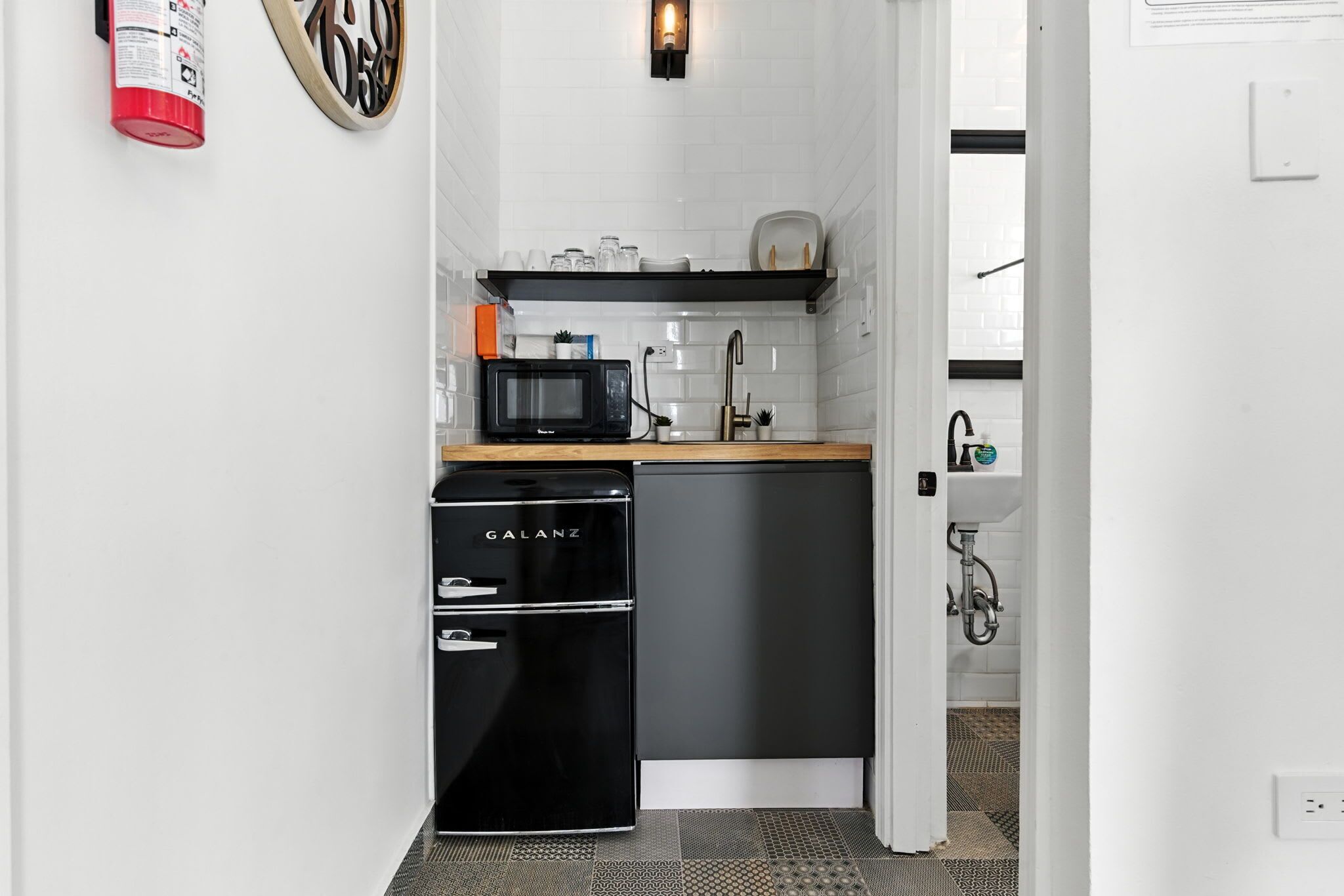 Een kleine keuken met een zwarte koelkast, een magnetron en een spoelbak.
