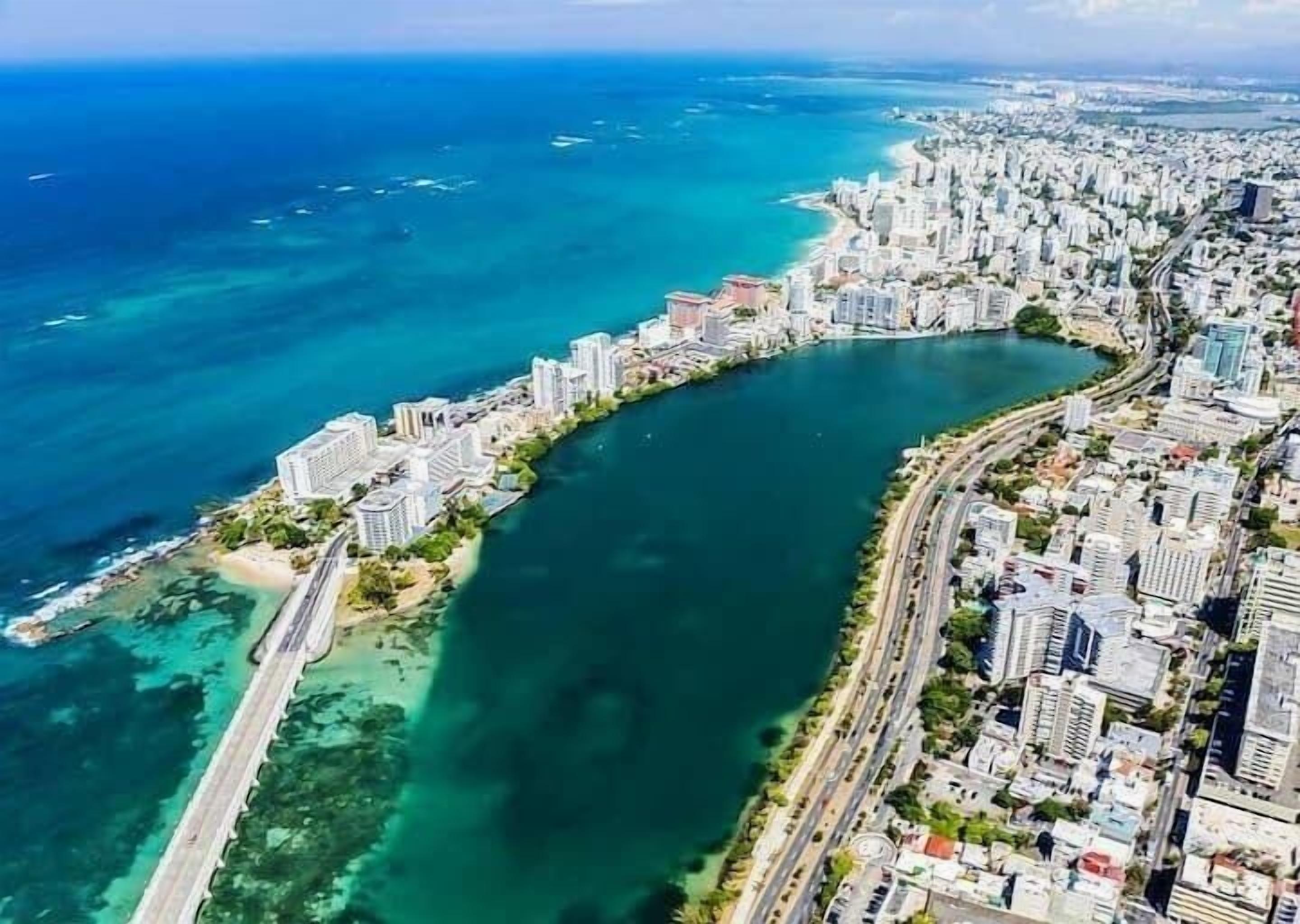 An aerial view of a coastal city with a curved bay, high-rise buildings, and a road parallel to the water.