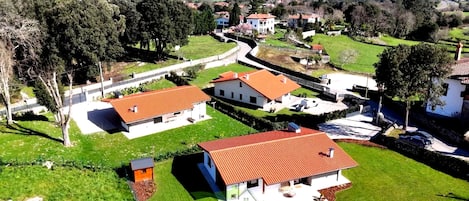 A residential area with houses featuring red-tiled roofs, surrounded by greenery and a clear view of the sea.