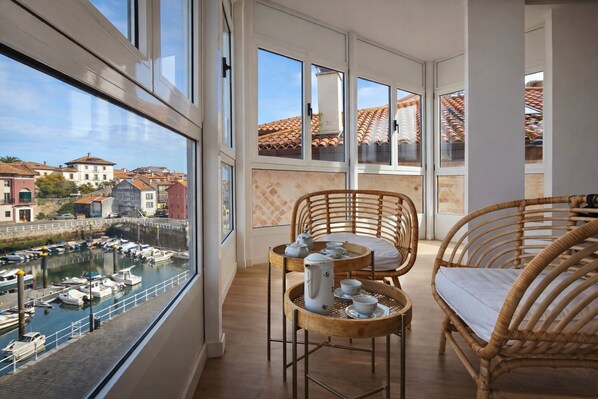 A balcony with wicker furniture, a table with tea set, and a view of a marina and buildings. - Llanes Downtown Apartment with Harbor View - Vega 3 (Llanes)