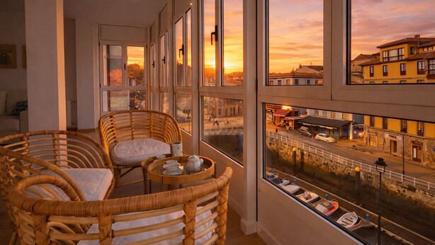 Varanda com cadeiras de vime e uma mesa, com vista para uma rua com edifícios e barcos.