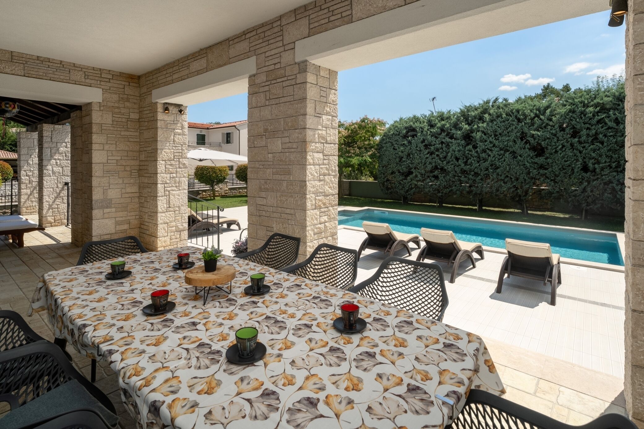 Un patio al aire libre con piscina, pilares de piedra y una mesa dispuesta con sillas y velas.