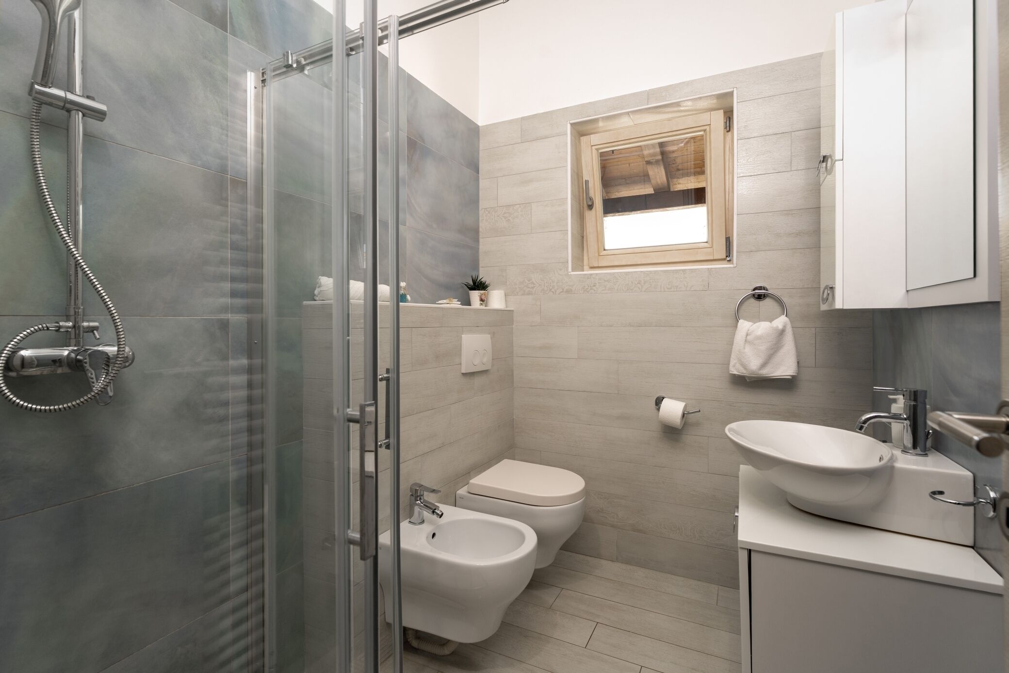 A modern bathroom with a glass shower enclosure, a bidet, a toilet, and a sink with a vessel basin.