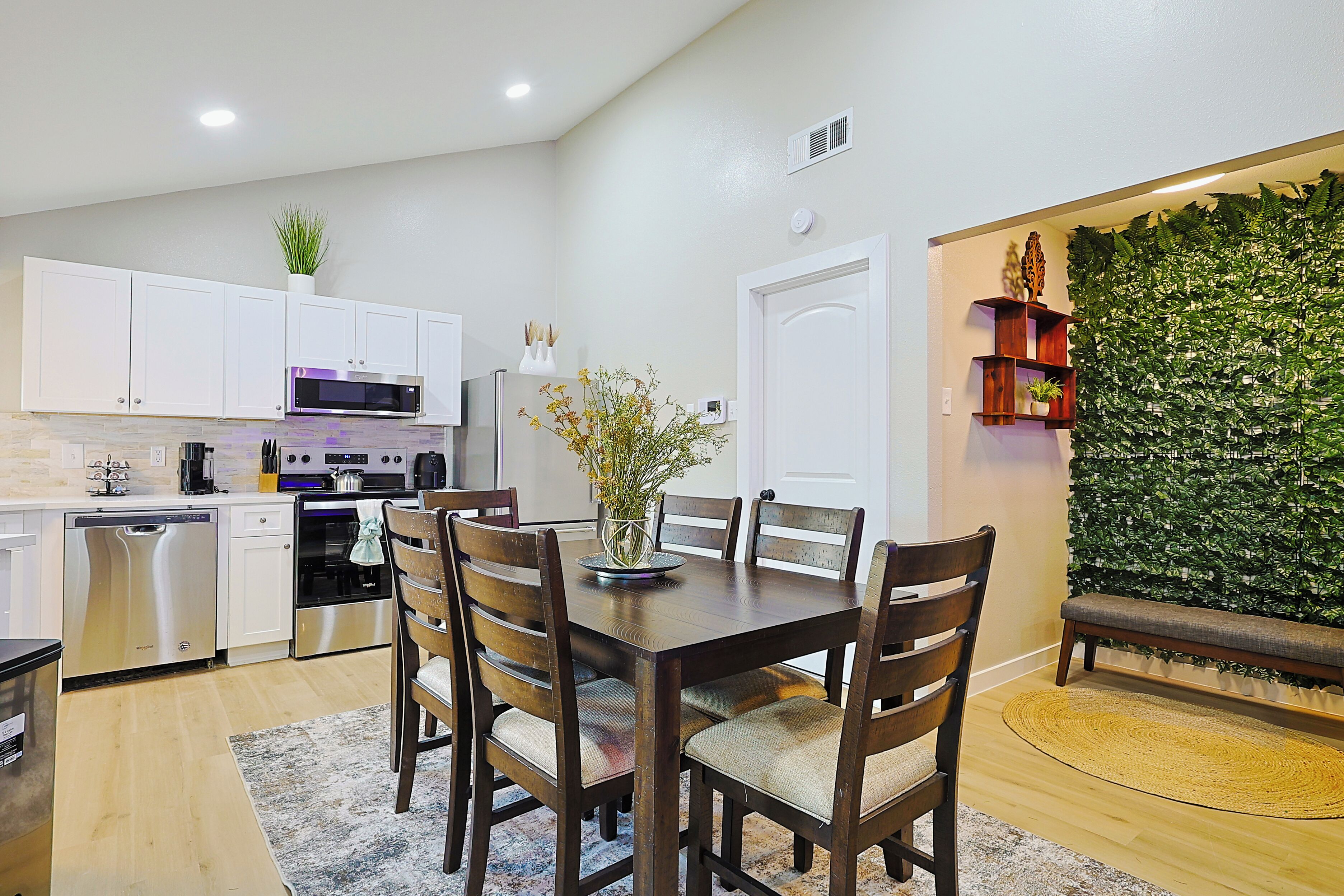 A modern kitchen with white cabinets, stainless steel appliances, and a dining area with wooden chairs and a table.