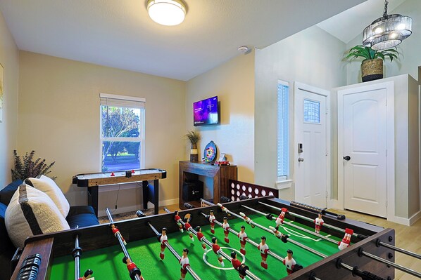 A room with a foosball table, a television mounted on the wall, and a door with a window.