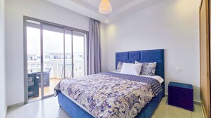 A bedroom with a large bed, a sliding glass door to a balcony, and a modern ceiling light.