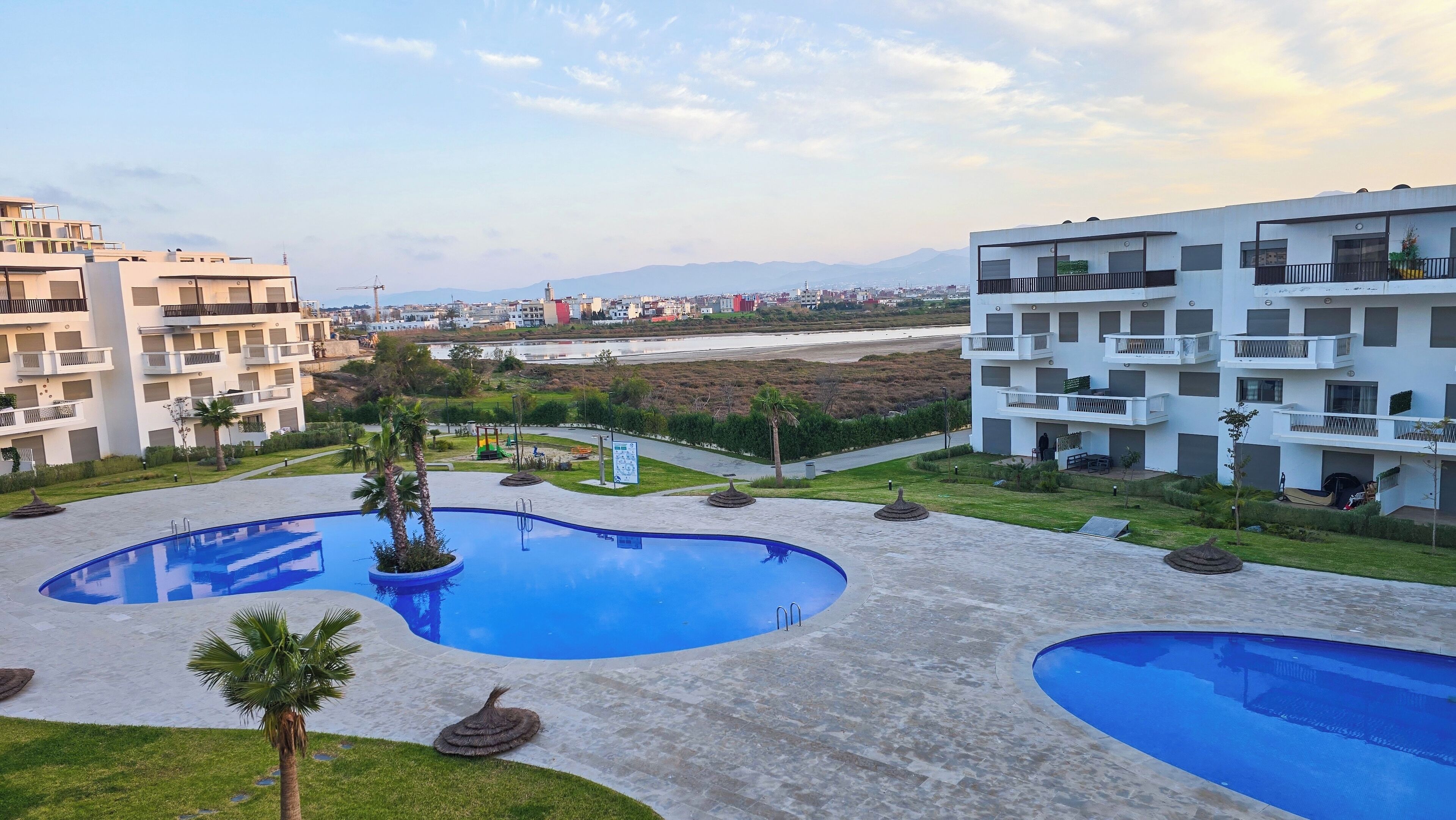 Zona residencial con modernos edificios de apartamentos, una piscina y vista a un horizonte urbano distante.
