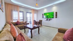 A modern living room with a sofa set, a dining table, and a TV mounted on the wall.