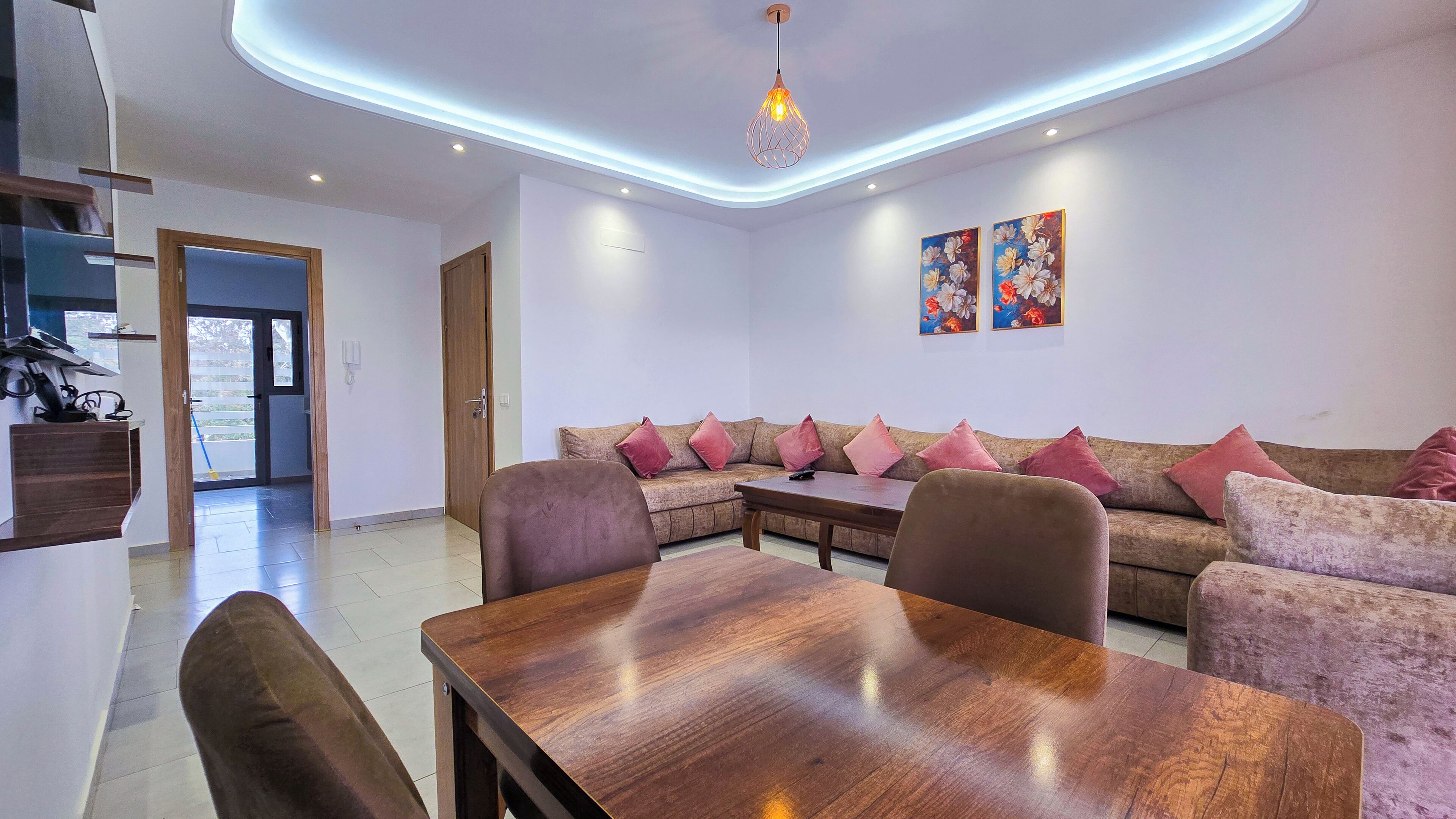 A modern living room with a wooden dining table, a sofa set, and a ceiling light fixture.