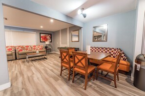 A living room with a sofa, a dining table with chairs, a billiards table, and a trash can.