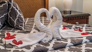 Ein Bett mit einem gemusterten Überwurf, zwei handgeschöpfte Seetangrosen aus Handtüchern und rote Rosenblätter.