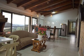 A spacious living area with a sofa, dining table, and chairs, a kitchen area with a refrigerator, and large windows offering a view of the outdoors.