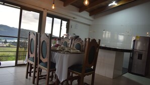 Un coin repas avec une table dressée pour quatre personnes, entouré de chaises élégantes, une cuisine moderne aux carreaux blancs et une vue sur un lac par de grandes fenêtres.
