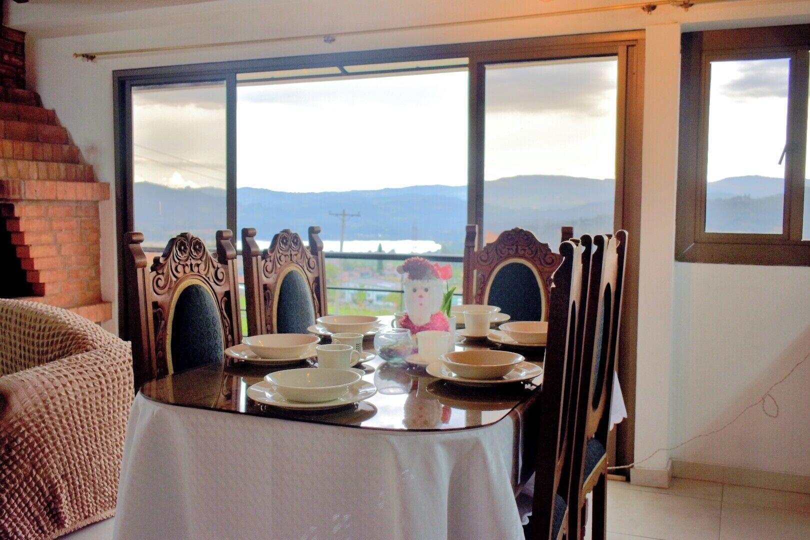 A dining table set with plates, cups, and a decorative item, with a view of mountains through large windows.