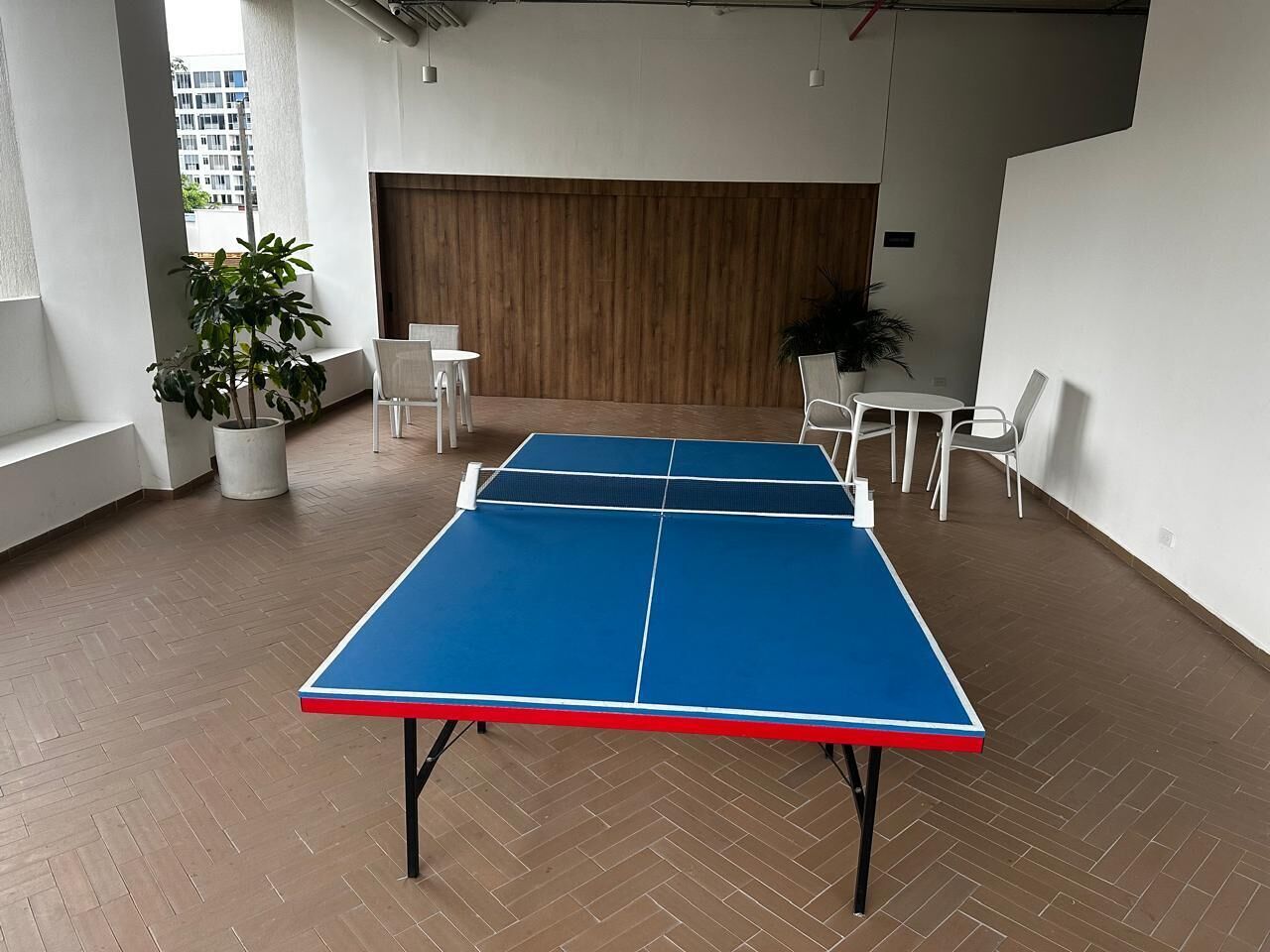 Una mesa de ping pong en una habitación con paredes blancas, un panel de madera y un suelo con patrón de espiga.