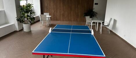 Una mesa de ping pong en una habitación con paredes blancas, un panel de madera y un suelo con patrón de espiga.
