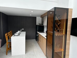 A modern kitchen with a central island, wooden cabinets, and a glass-fronted wine rack.