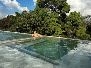 A man relaxing in a clear infinity pool with a view of dense foliage and a clear sky. - LUXURY DUPLEX VILLA (Armenia)