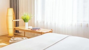 A neatly arranged hotel room with a bed, a bedside table with a vase of flowers, a lamp, and a window with sheer curtains. - TRANQUIL HOUSE (Lhasa)