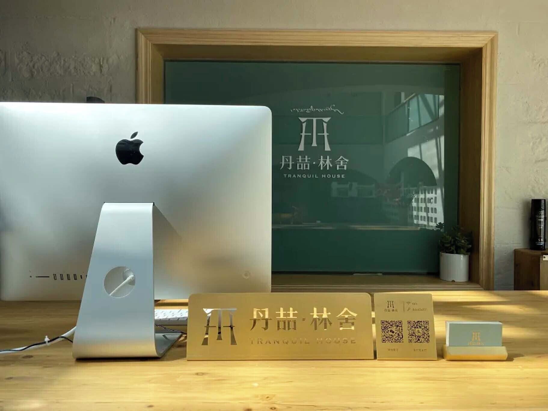 A wooden desk with a MacBook, a MacBook stand, and a framed sign with Chinese characters.