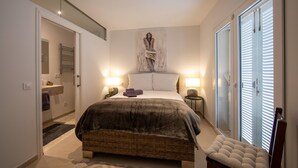 A bedroom with a large bed, two bedside lamps, a wall-mounted artwork, and a view through the window blinds. - Beautiful home in Portocolom (Portocolom)