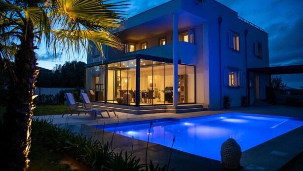 A modern two-story house with a swimming pool, glass doors leading to a patio, and a well-lit interior. - Beautiful home in Portocolom (Portocolom)