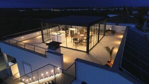 A modern rooftop terrace with a glass-enclosed dining area, a seating area, and a staircase leading to an upper level. - Beautiful home in Portocolom (Portocolom)