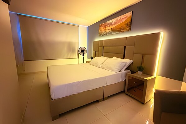 Een moderne slaapkamer met een groot bed, een nachtkastje met lamp en een kunstwerk aan de muur.