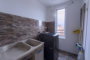 Een badkamer met een stenen muur, een wastafel, een wasmachine en een dweil die tegen de muur staat.