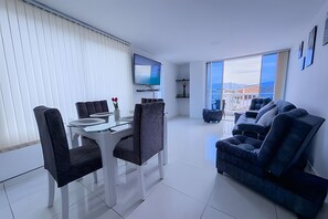 Een moderne woonkamer met een eethoek, een bank en een aan de muur bevestigde televisie.