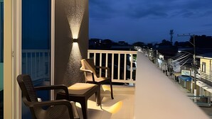 Un balcon avec une chaise et une table, une balustrade et une vue sur le paysage urbain au crépuscule.