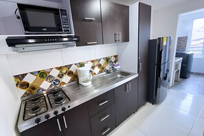 Een moderne keuken met donkere kastjes, een roestvrijstalen aanrecht, een gasfornuis, een magnetron en een koelkast.