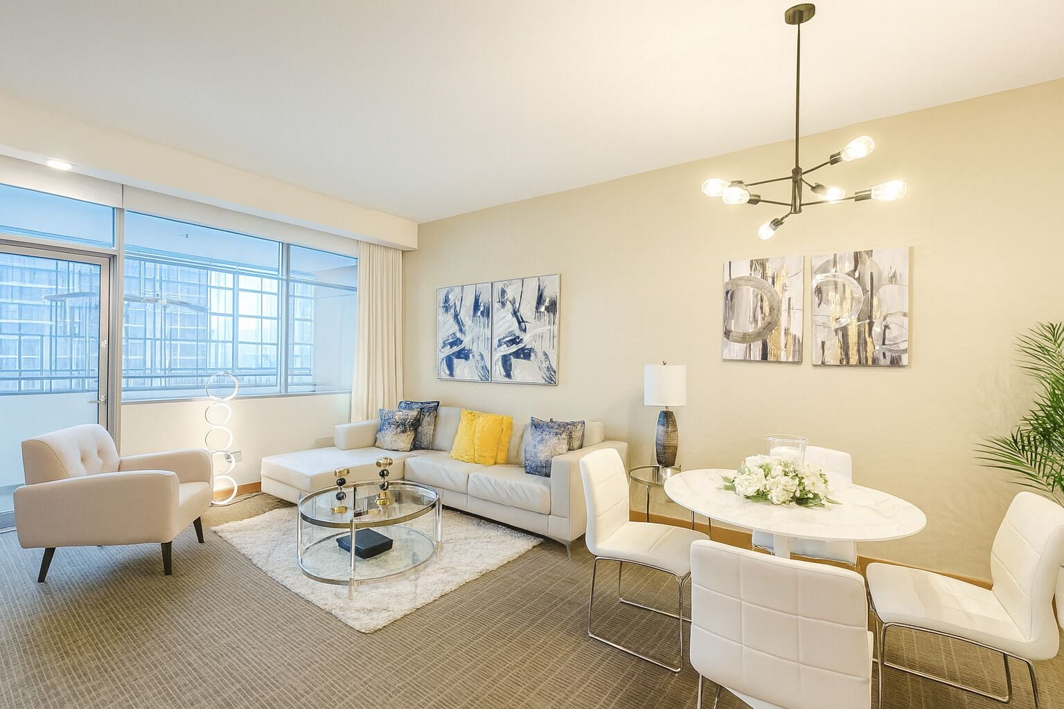 A modern living room with a sofa, coffee table, and chairs, a dining table with flowers, and artwork on the walls.