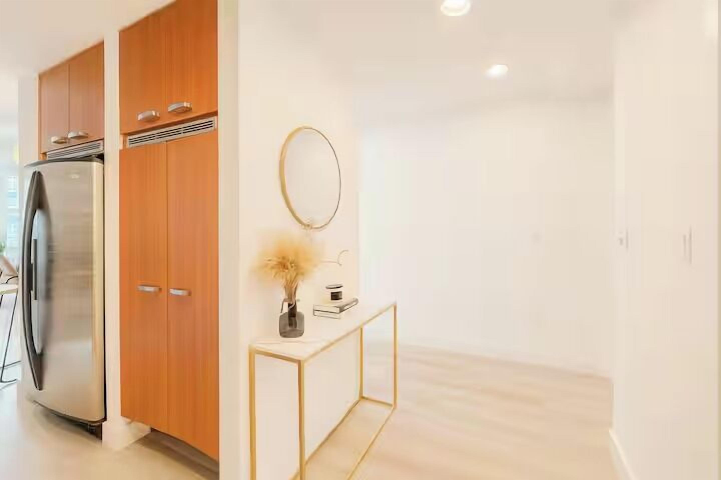 A modern kitchen with wooden cabinets, a stainless steel refrigerator, and a gold-framed console table with a vase and book.