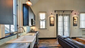 A modern kitchen with a large sink, stove, and a dining area with a leather couch and wooden table. - The Penthouse Suite - South Main Escape (Buena Vista)