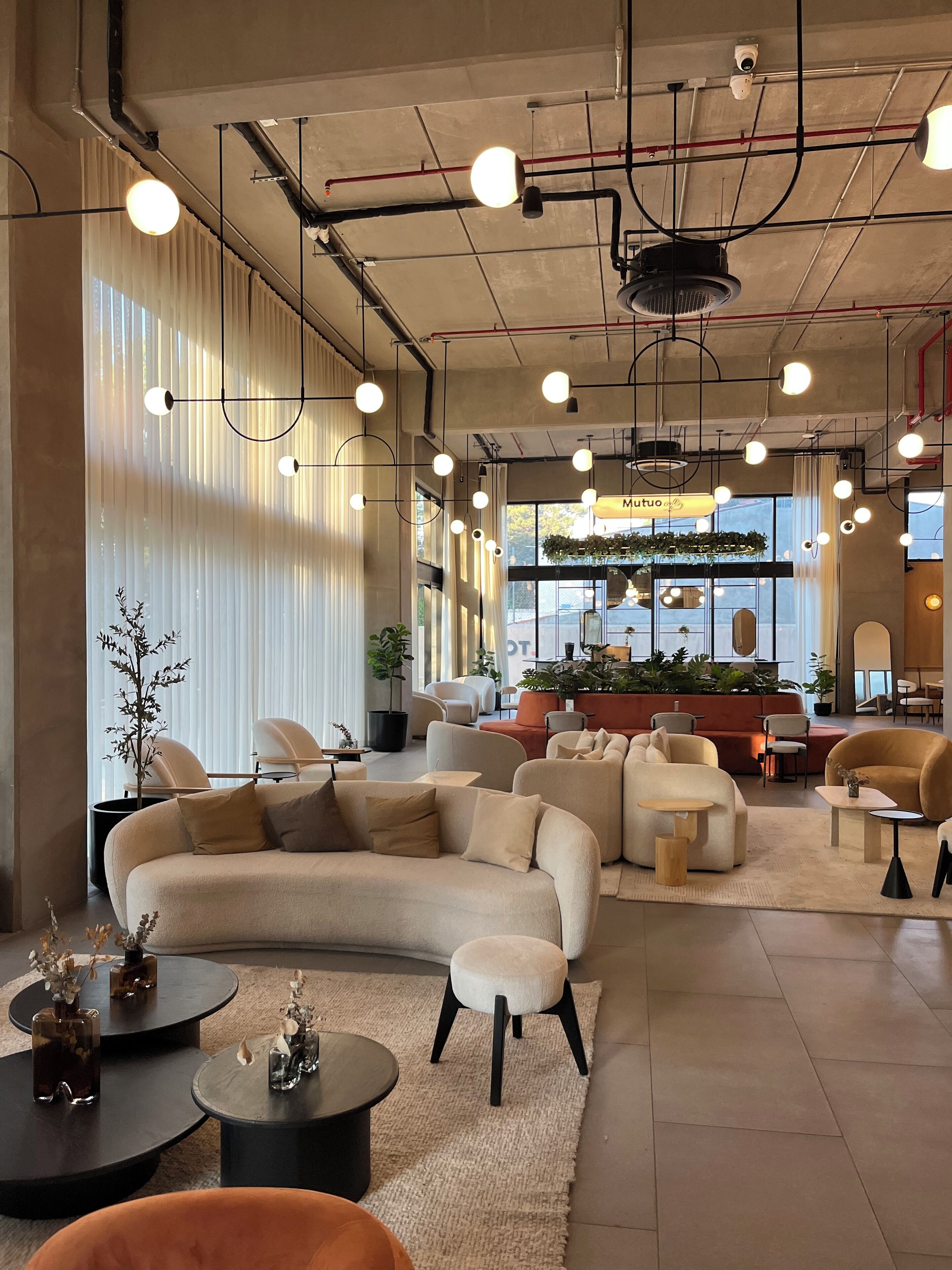 Eine geräumige Lobby mit einer gebogenen Couch, verschiedenen Sitzbereichen und einer Kaffeebar im Hintergrund.