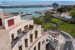 A coastal building with a rooftop terrace, a view of the sea, and a parking area with a curved road. - Stay In St. Catarina Park, by PAUSA H. Rentals (Funchal)