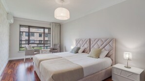 Ein modernes Schlafzimmer mit zwei Betten, einem großen Fenster und Blick auf Gebäude.
