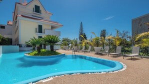Una piscina amb gandules i palmeres, envoltada d'edificis.