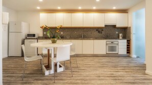Una cocina moderna con armarios blancos, encimera de granito, horno integrado y un comedor con mesa y sillas blancas.