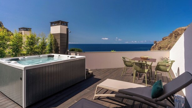 Una terraza en la azotea con un jacuzzi, mobiliario exterior y vistas al océano.