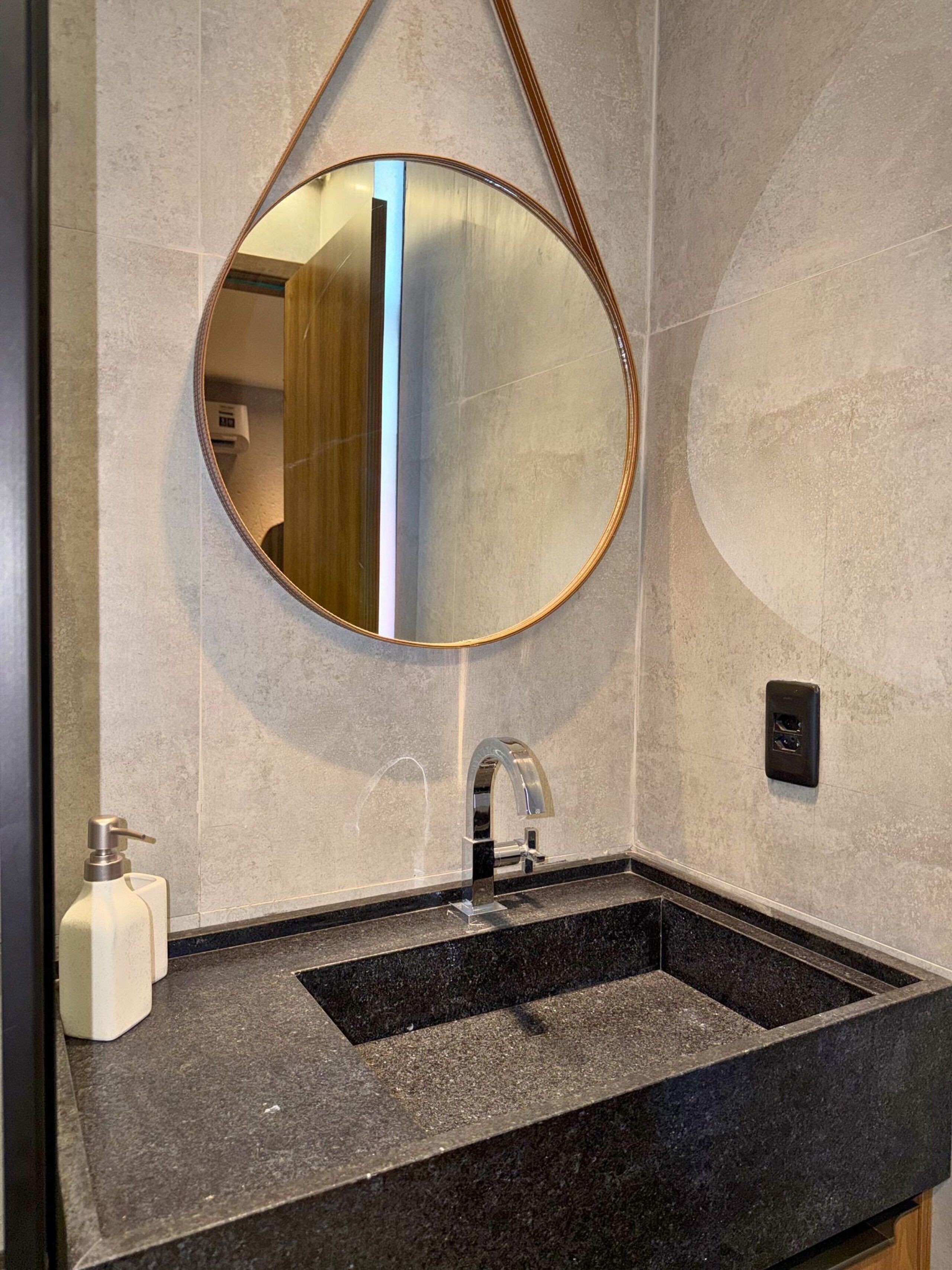 Une salle de bain avec un lavabo rectangulaire, un miroir rond et un distributeur de serviettes.